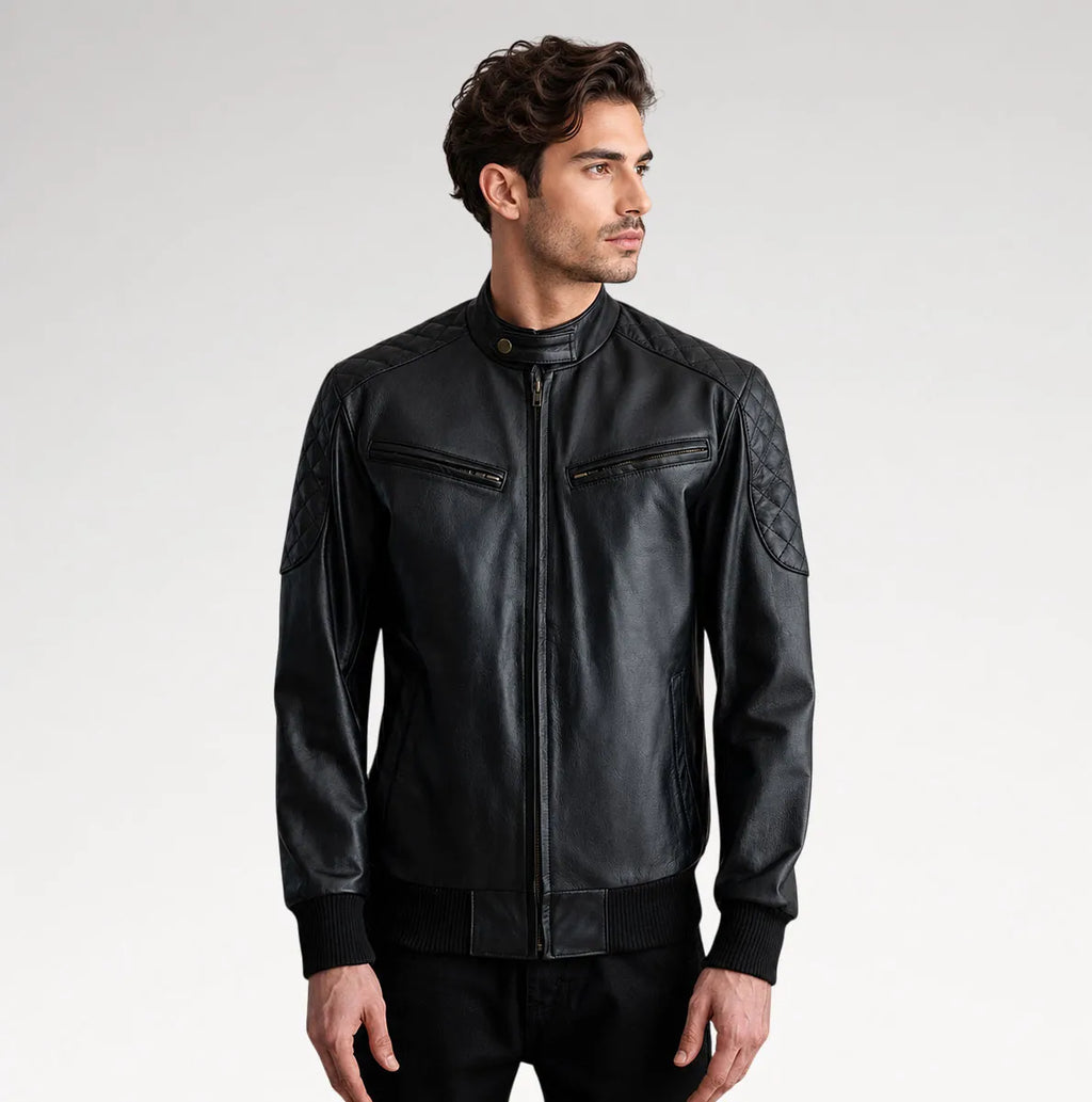 A man wearing a black leather jacket with quilted shoulder details, zippered chest pockets, and a stand-up collar, photographed against a light gray studio background.