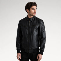 A man wearing a black leather jacket with quilted pattern details on the upper sleeves, photographed against a light gray studio background.