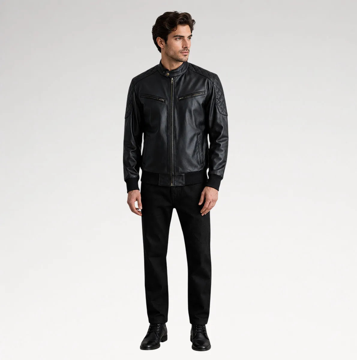 A man modeling a black leather jacket with zippered chest pockets and ribbed cuffs, paired with black pants and black shoes, against a light gray studio background.