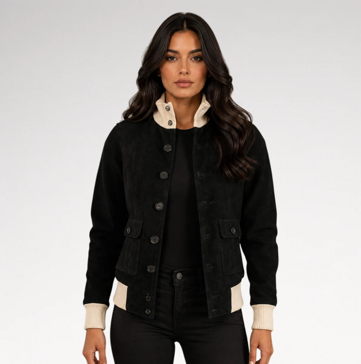 A woman modeling a black corduroy jacket with cream ribbed collar, cuffs, and hem, paired with black pants against a light gray studio background.
