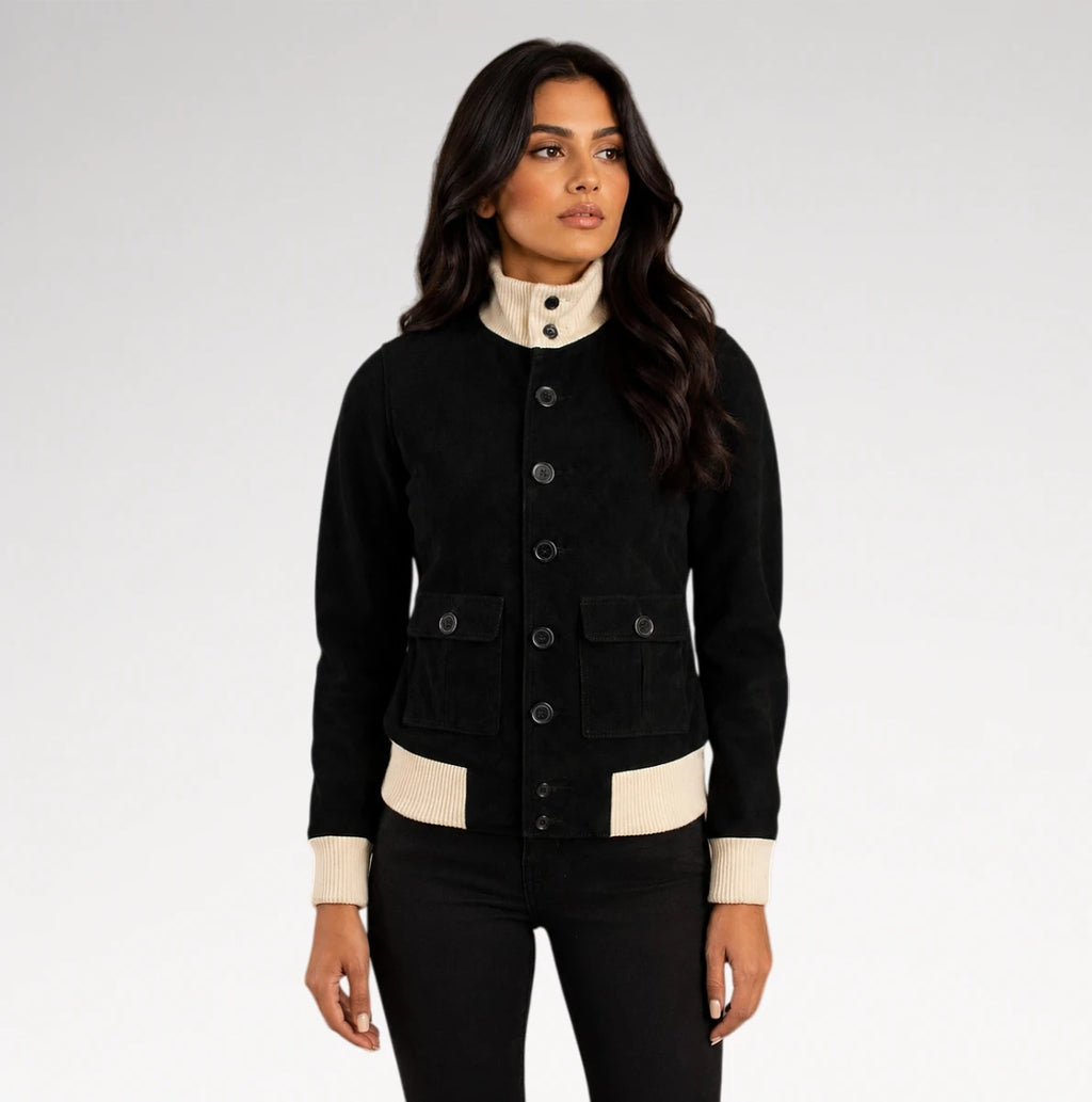 A woman modeling a black jacket with contrasting cream ribbed trim at the mock neck, cuffs, and hem, paired with black pants against a light gray studio background.