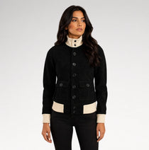 A woman modeling a black jacket with contrasting cream ribbed trim at the mock neck, cuffs, and hem, paired with black pants against a light gray studio background.