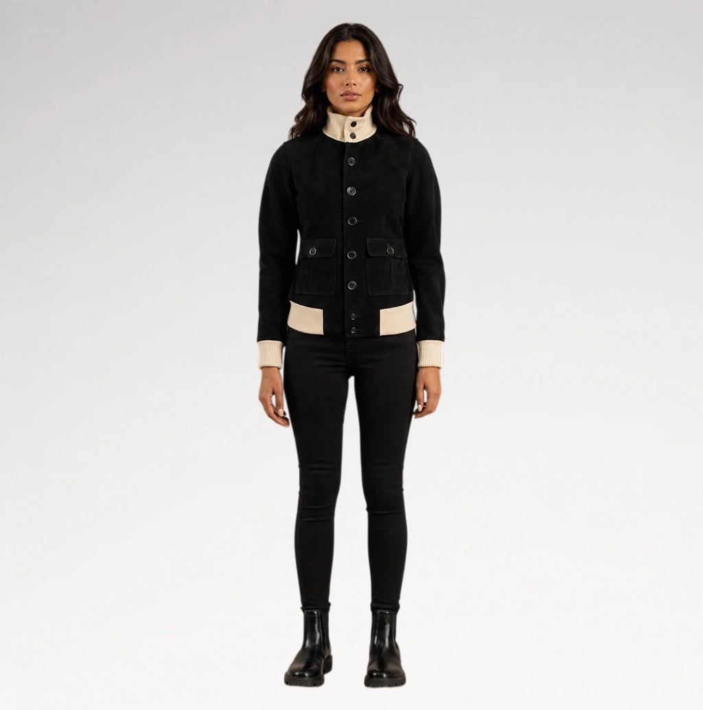 A model stands against a light gray studio background wearing a black cropped button-front jacket with beige contrast panels at the collar, cuffs, and hem, paired with black skinny pants and black ankle boots.