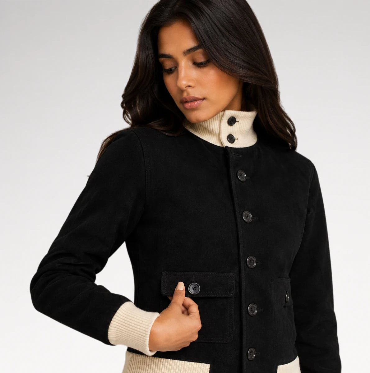 A woman wearing a black jacket with a cream ribbed mock neck and cuffs, shown against a light gray studio background.