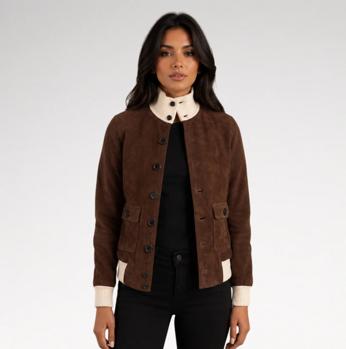 A woman modeling a brown suede jacket with a cream-colored collar, cuffs, and hem, worn over a black top and black pants against a light gray studio background.