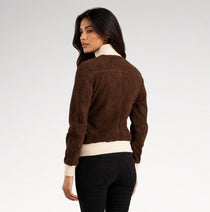 A woman shown from the back wearing a brown suede bomber-style jacket with cream ribbed trim at the collar and hem, paired with black pants, against a light gray studio background.