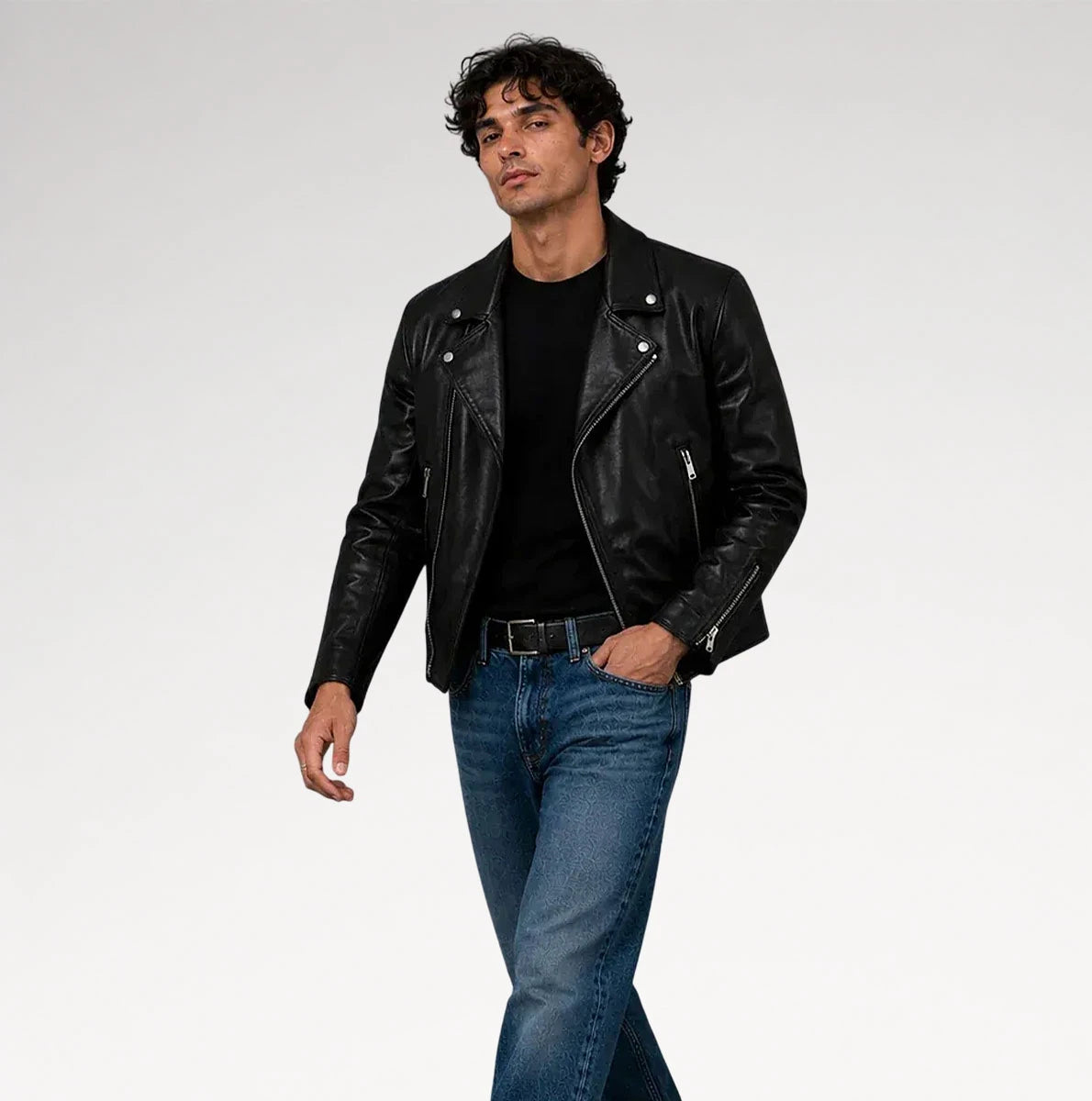 A man wearing a black leather moto jacket over a black t-shirt and blue jeans, standing against a light gray studio background. Main image