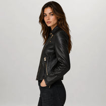 A woman wearing a black leather moto jacket with gold-tone zippers, shown in a side profile against a light gray studio background.