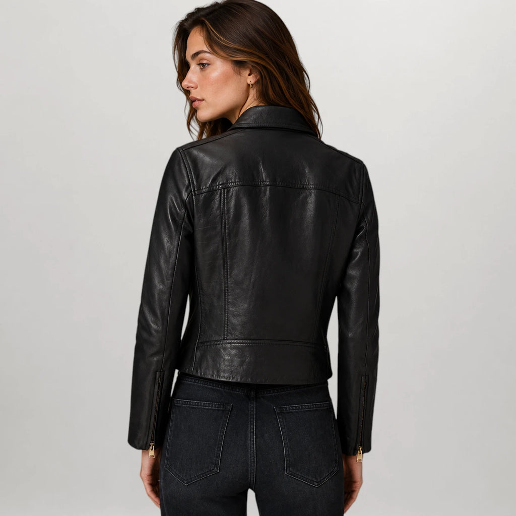 A woman shown from the back wearing a black leather moto jacket and dark jeans against a light gray studio background.