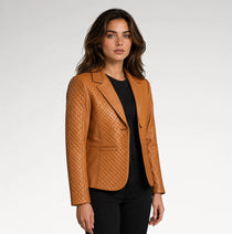 A woman modeling a tan quilted leather blazer over a black top and black pants, photographed against a light gray studio background.