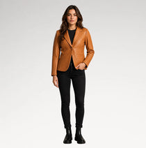 A woman modeling a tan quilted blazer over a black top and black skinny pants, standing against a light gray studio background.