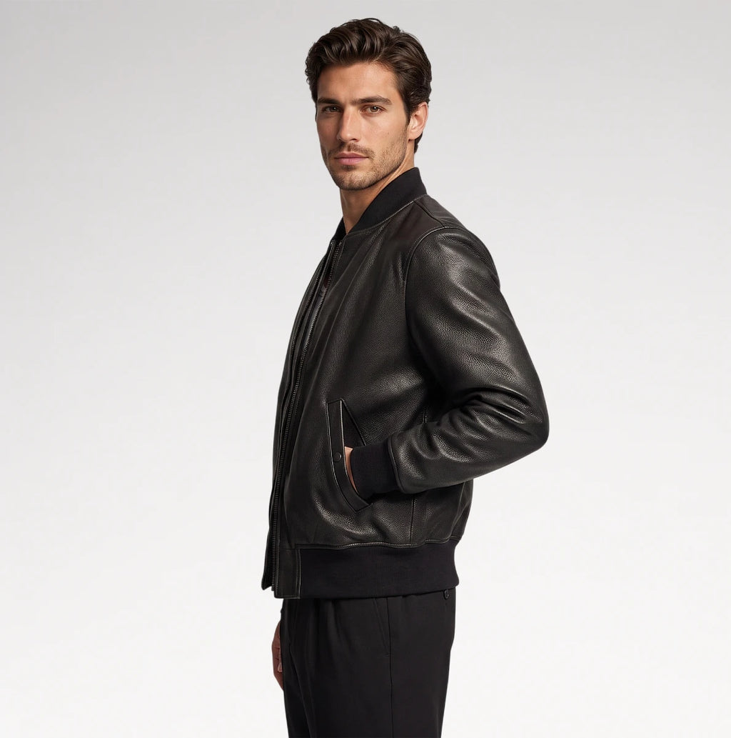 A man wearing a black leather bomber jacket and black pants, shown in profile against a light gray studio background.