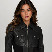 A woman wearing a black leather jacket with a silver zipper and snap-button chest pockets, photographed against a plain light gray studio background.