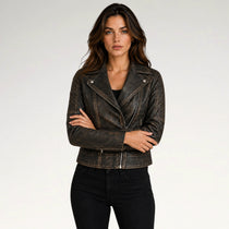 A woman modeling a distressed dark brown leather moto jacket with silver snap and zip details, paired with black jeans, against a plain light gray background.