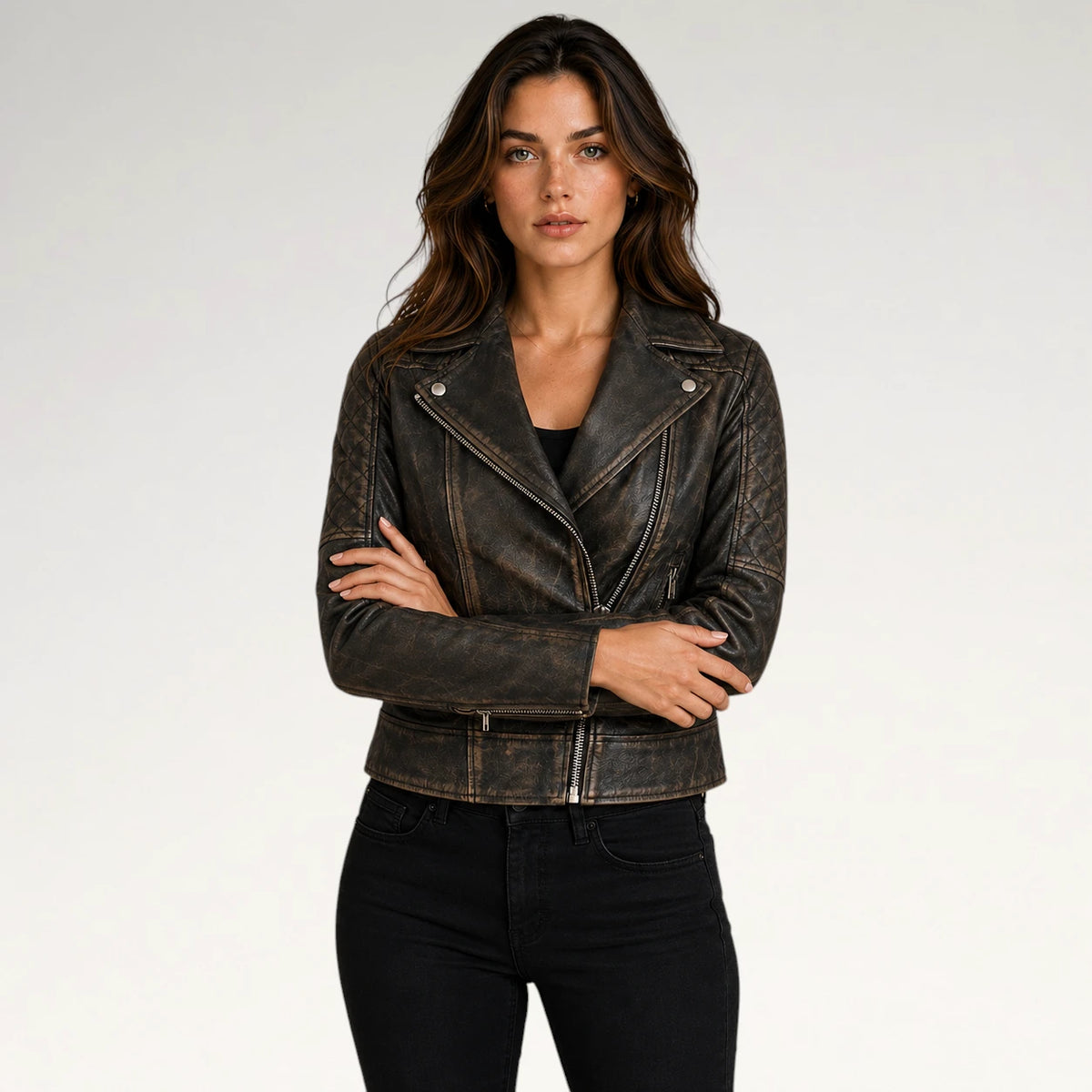 A woman modeling a distressed dark brown leather moto jacket with silver snap and zip details, paired with black jeans, against a plain light gray background.
