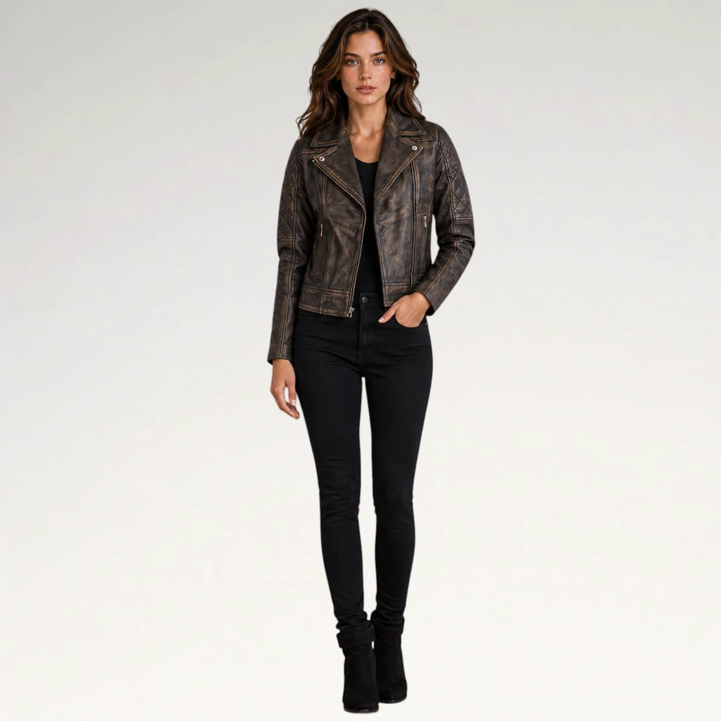 A woman modeling a distressed brown faux-leather moto jacket with gold-tone hardware, paired with black skinny jeans and black ankle boots, against a plain white studio background.
