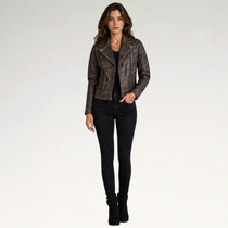 A woman modeling a distressed brown faux-leather moto jacket with gold-tone hardware, paired with black skinny jeans and black ankle boots, against a plain white studio background.