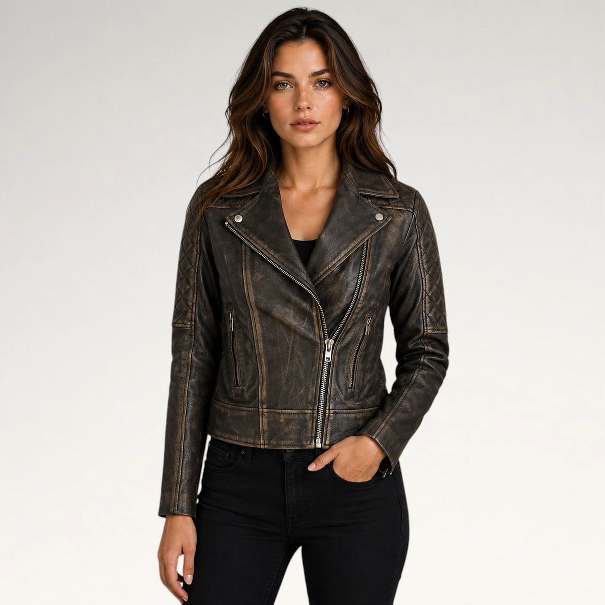 A woman modeling a distressed dark brown faux leather moto jacket with silver hardware, paired with black jeans, against a light gray studio background.