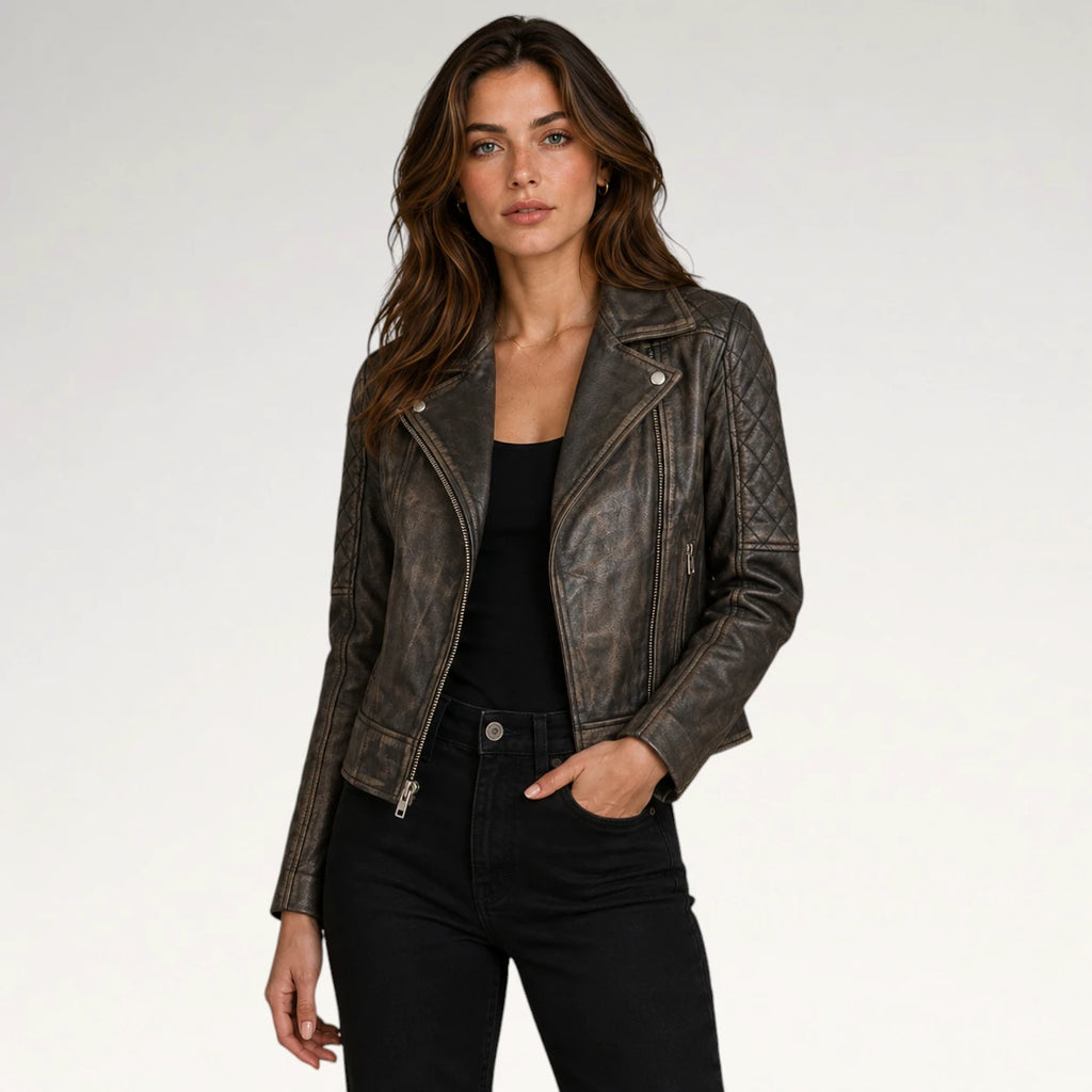 A woman modeling a distressed dark brown leather moto jacket with silver hardware, worn over a black top and black jeans, against a plain light gray studio background.
