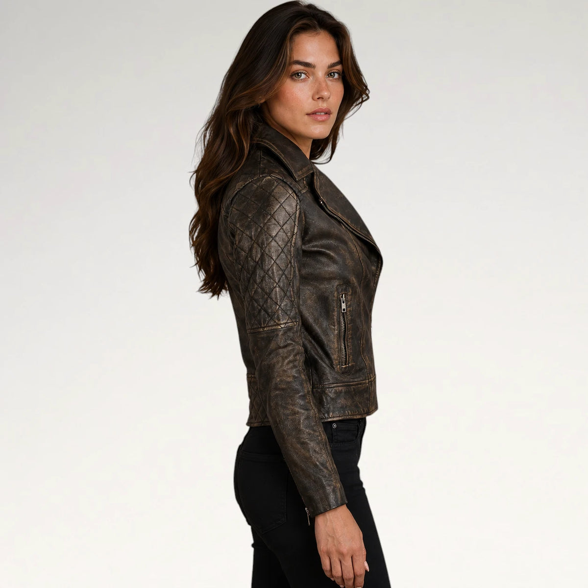 A woman wearing a distressed brown leather motorcycle jacket with quilted shoulder panels, shown in profile against a plain light gray studio background.