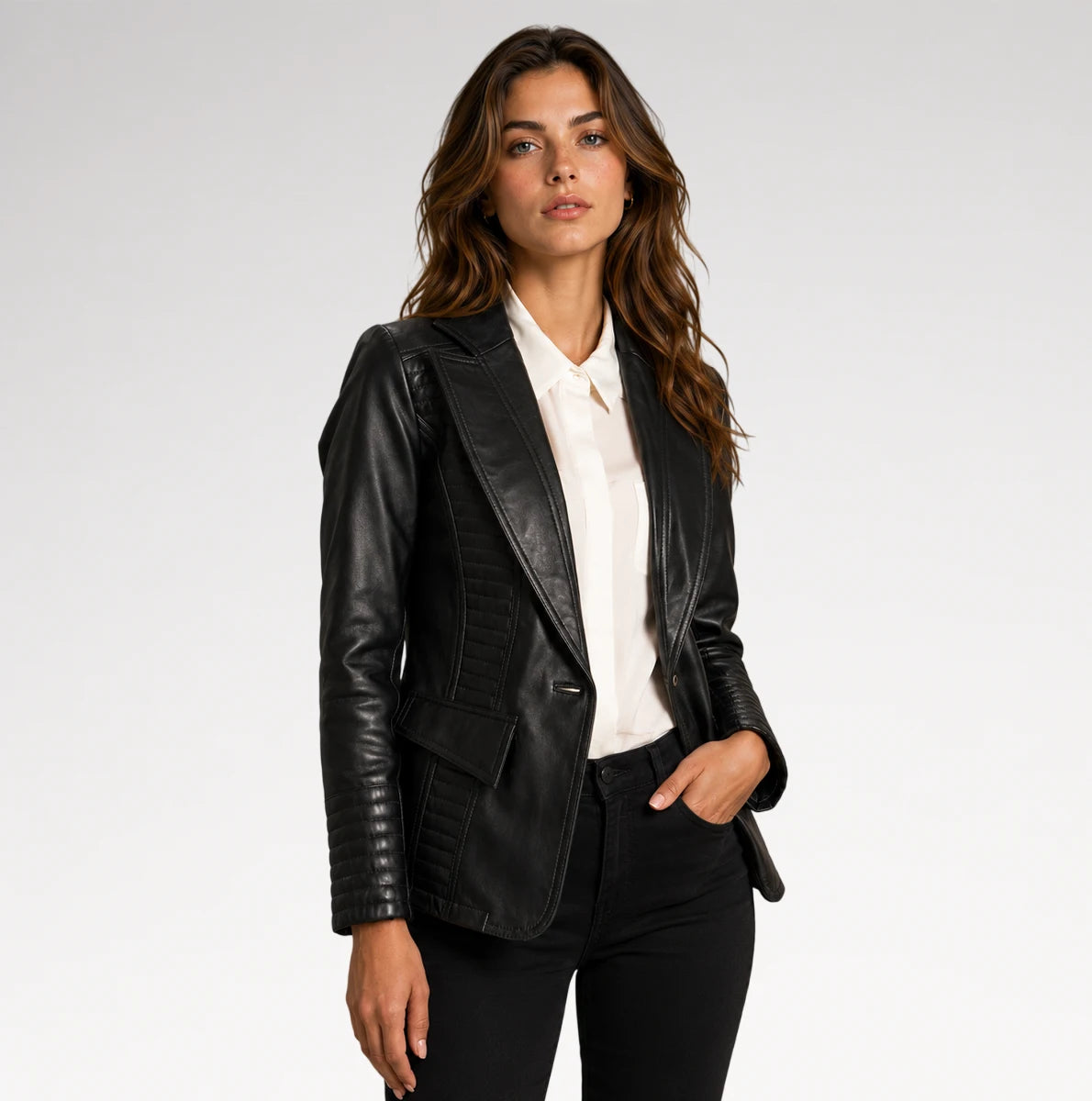 A woman modeling a black faux-leather blazer with quilted panel details, worn open over a white collared shirt and black pants, against a light gray studio background.