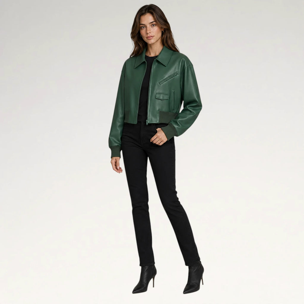 A woman modeling a dark green leather jacket over a black top and black skinny pants, paired with black ankle boots, against a plain light gray studio background.