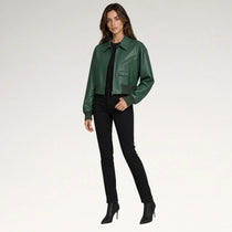 A woman modeling a dark green leather jacket over a black top and black skinny pants, paired with black ankle boots, against a plain light gray studio background.