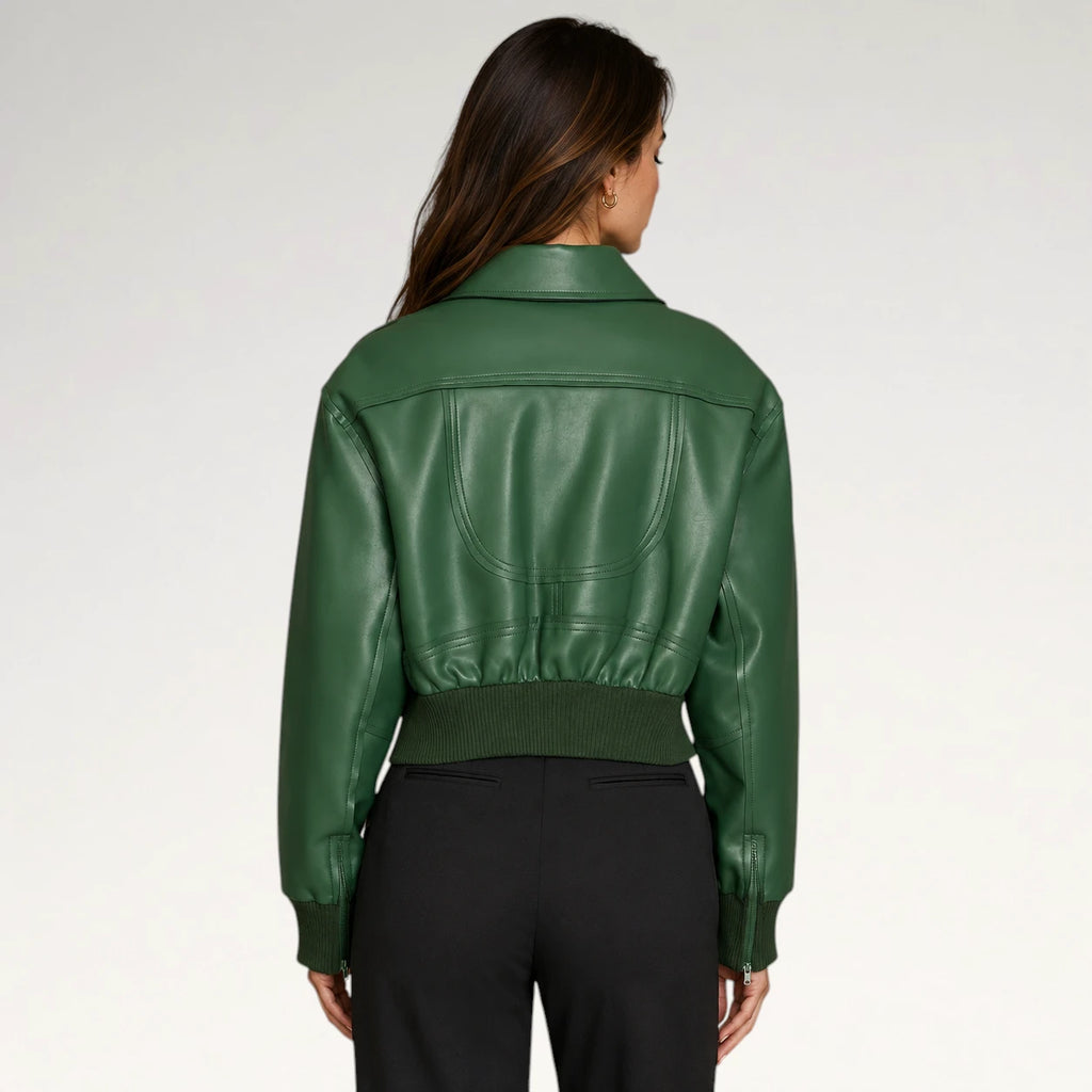 A woman viewed from the back wearing a cropped green faux-leather jacket with a ribbed hem and cuffs, paired with black pants, against a light gray studio background.