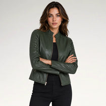 A woman modeling a dark olive green faux leather jacket with a stand collar and front zipper, paired with a black top and black pants, against a light gray studio background.