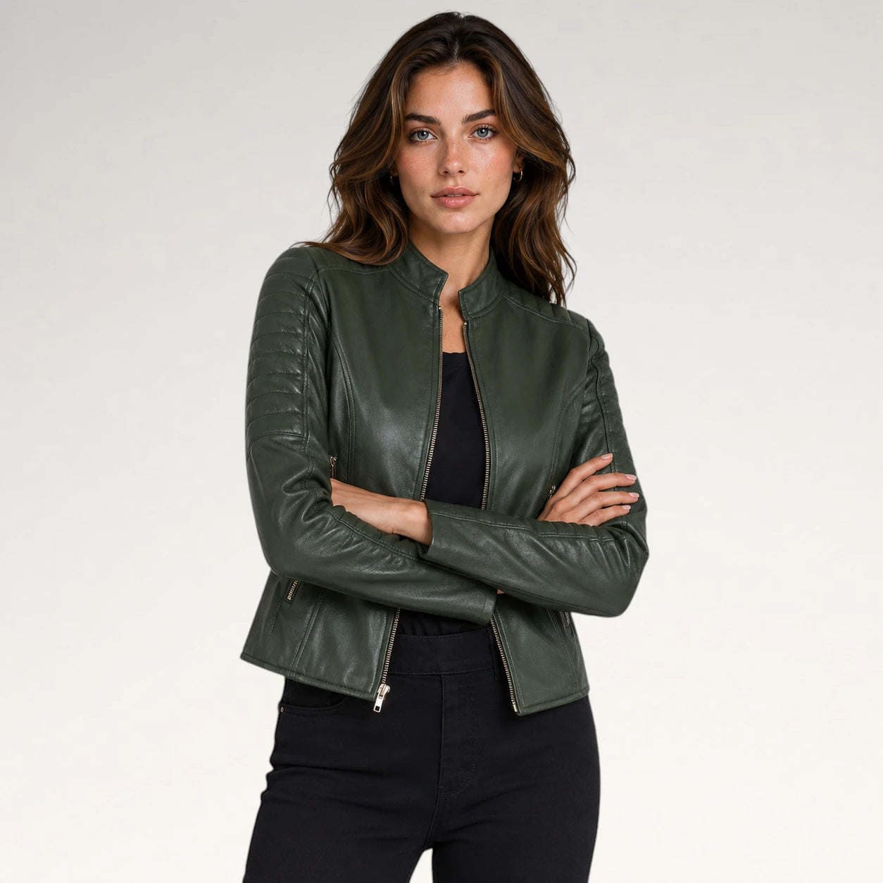 A woman modeling a dark olive green faux leather jacket with a stand collar and front zipper, paired with a black top and black pants, against a light gray studio background.