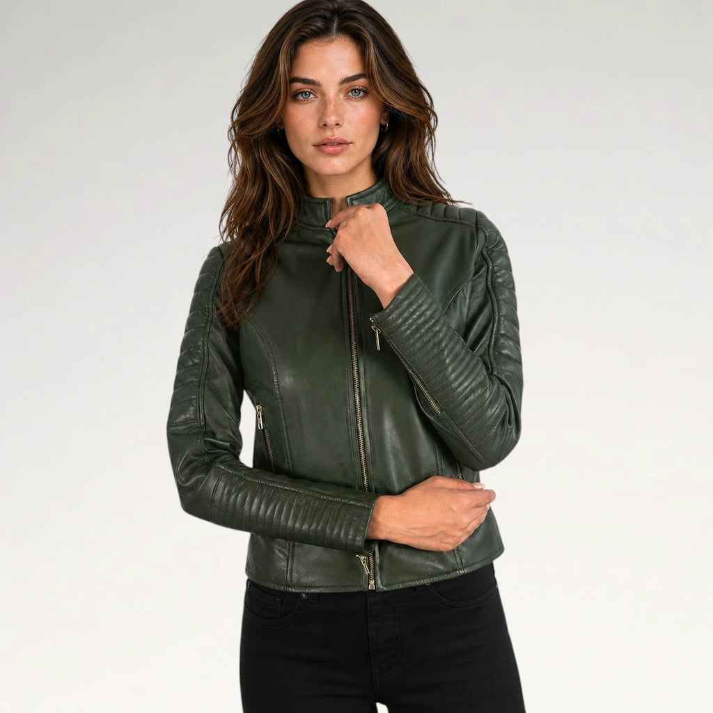 A woman modeling a dark olive green faux leather biker jacket with gold-tone zippers, paired with black jeans, against a plain light gray studio background.