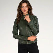 A woman modeling a dark olive green faux leather biker jacket with gold-tone zippers, paired with black jeans, against a plain light gray studio background.