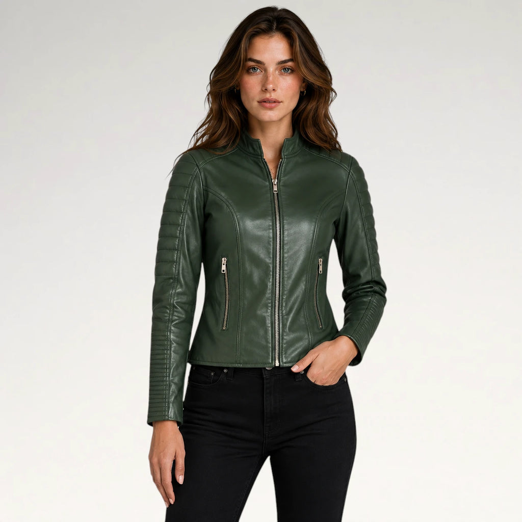 A woman modeling a dark green faux leather moto jacket with quilted sleeve panels and silver zippers, paired with black jeans against a light gray studio background.