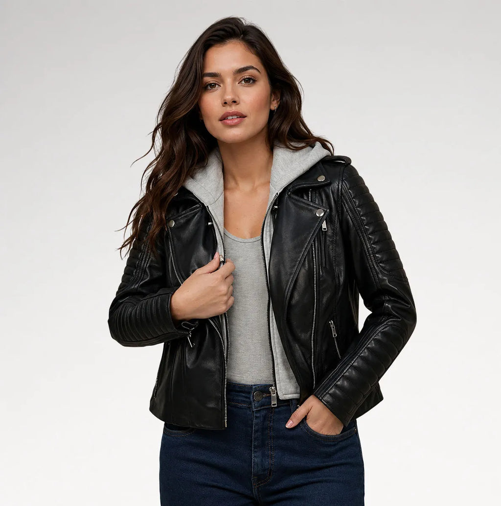 A woman modeling a black leather moto jacket with a gray hood, worn over a gray tank top and dark blue jeans, against a light gray studio background.
