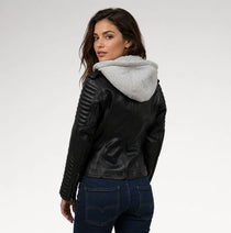 A woman wearing a black faux leather moto jacket with a light gray heathered hood, paired with dark blue jeans, photographed against a light gray studio background.