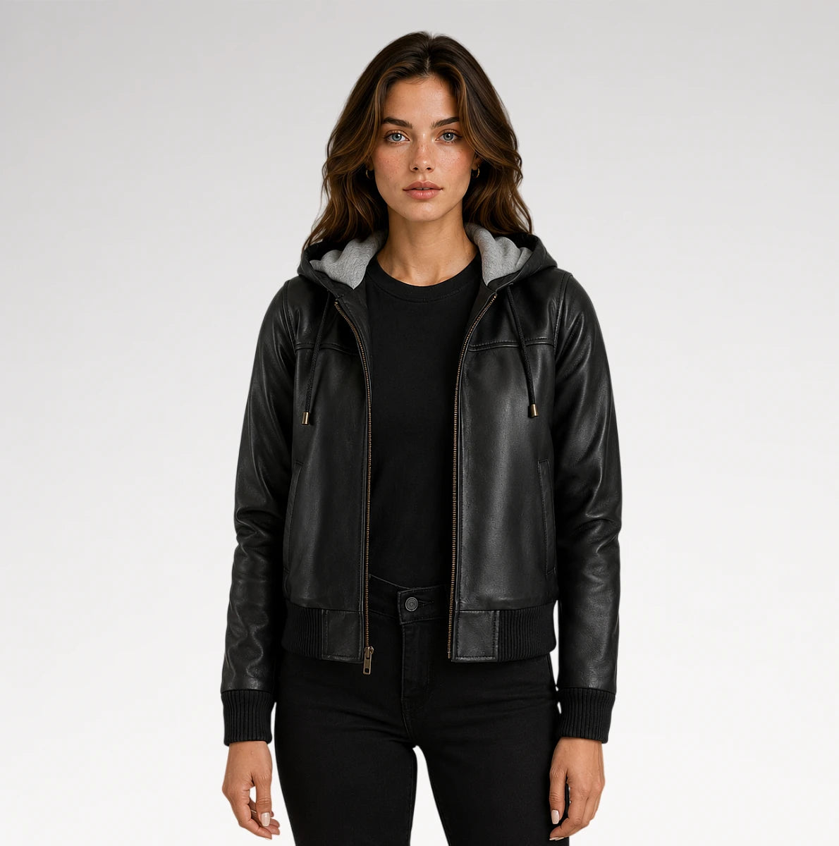 A woman modeling a black faux-leather hooded jacket with a gray fleece-lined hood, worn over a black top and black pants against a light gray studio background. Main image