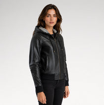 A woman wearing a black faux-leather hooded jacket with a gray hood lining, black ribbed knit trim, and a front zipper, photographed against a light gray studio background.
