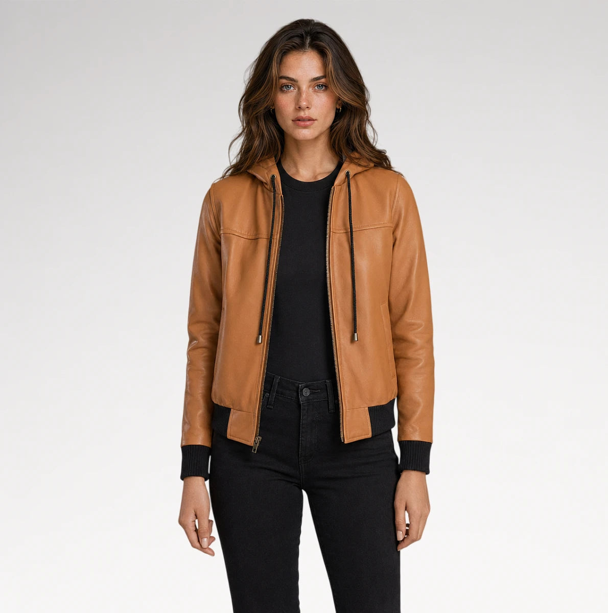 A woman modeling a tan leather hooded jacket with a front zipper, black ribbed cuffs and hem, worn over a black top and black jeans against a light gray studio background. Main image