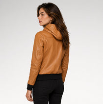 A woman shown from the back wearing a cropped tan faux-leather hooded jacket with black ribbed hem and cuffs, paired with black pants, against a light gray studio background.