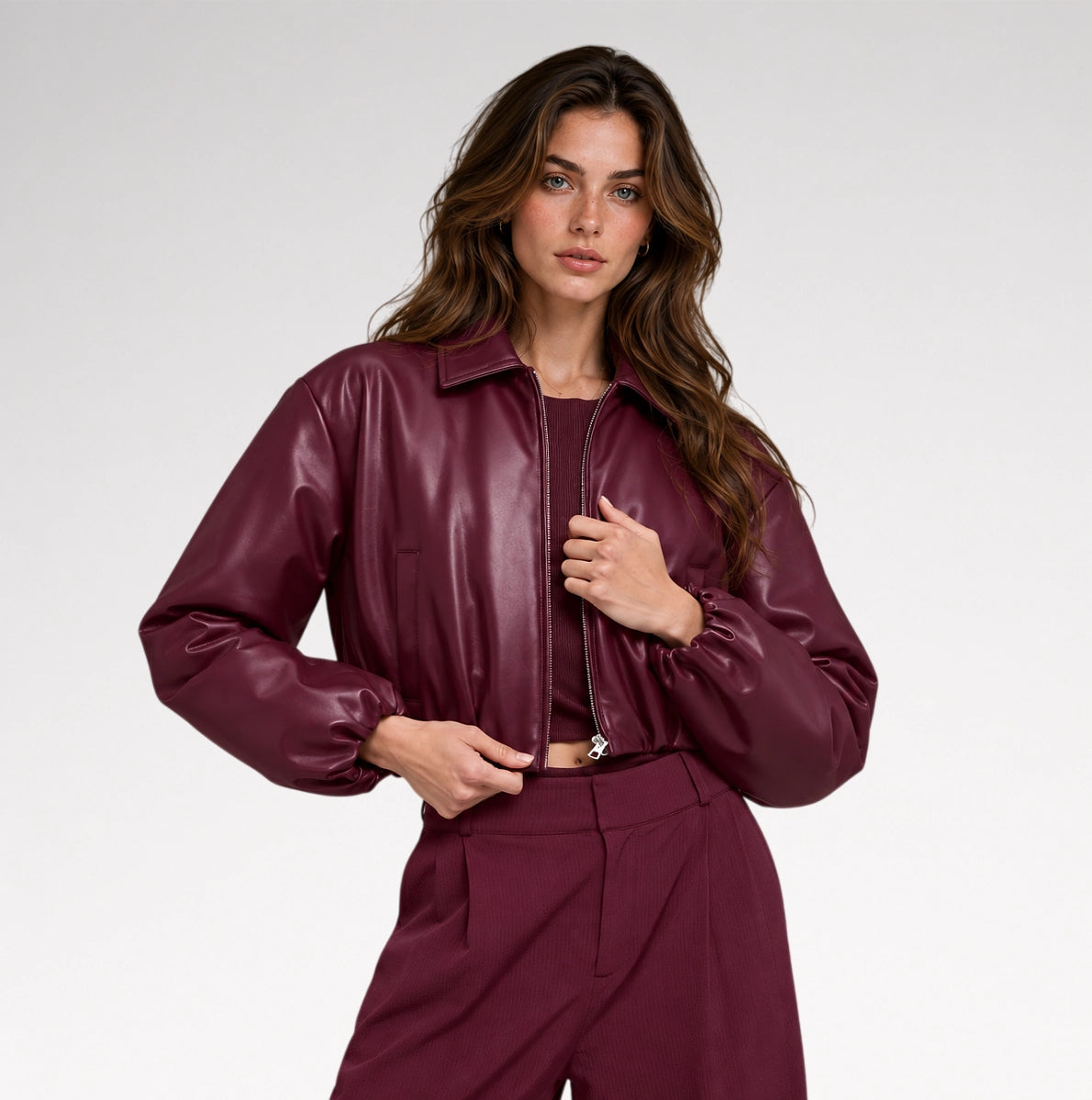 A woman wearing a glossy, deep burgundy faux-leather cropped jacket and matching trousers, photographed from the side against a clean white studio background. Main image