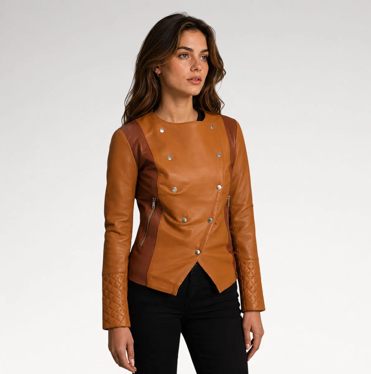 A woman modeling a tan faux-leather jacket with quilted sleeves and silver snap details, paired with black pants, against a light gray studio background.