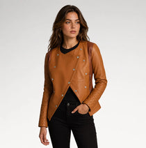 A woman modeling a tan leather jacket with silver-tone snap buttons and quilted sleeves, paired with a black top and black pants, against a light gray studio background.