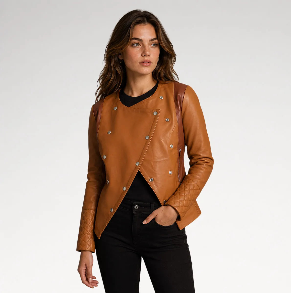 A woman modeling a tan leather jacket with silver-tone snap buttons and quilted sleeves, paired with a black top and black pants, against a light gray studio background.