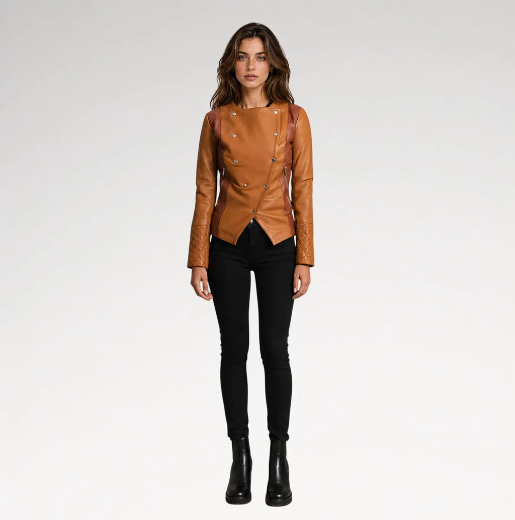 A woman modeling a tan leather moto jacket with silver-tone studs and double-breasted buttons, paired with black skinny pants and black ankle boots, against a light gray studio background.