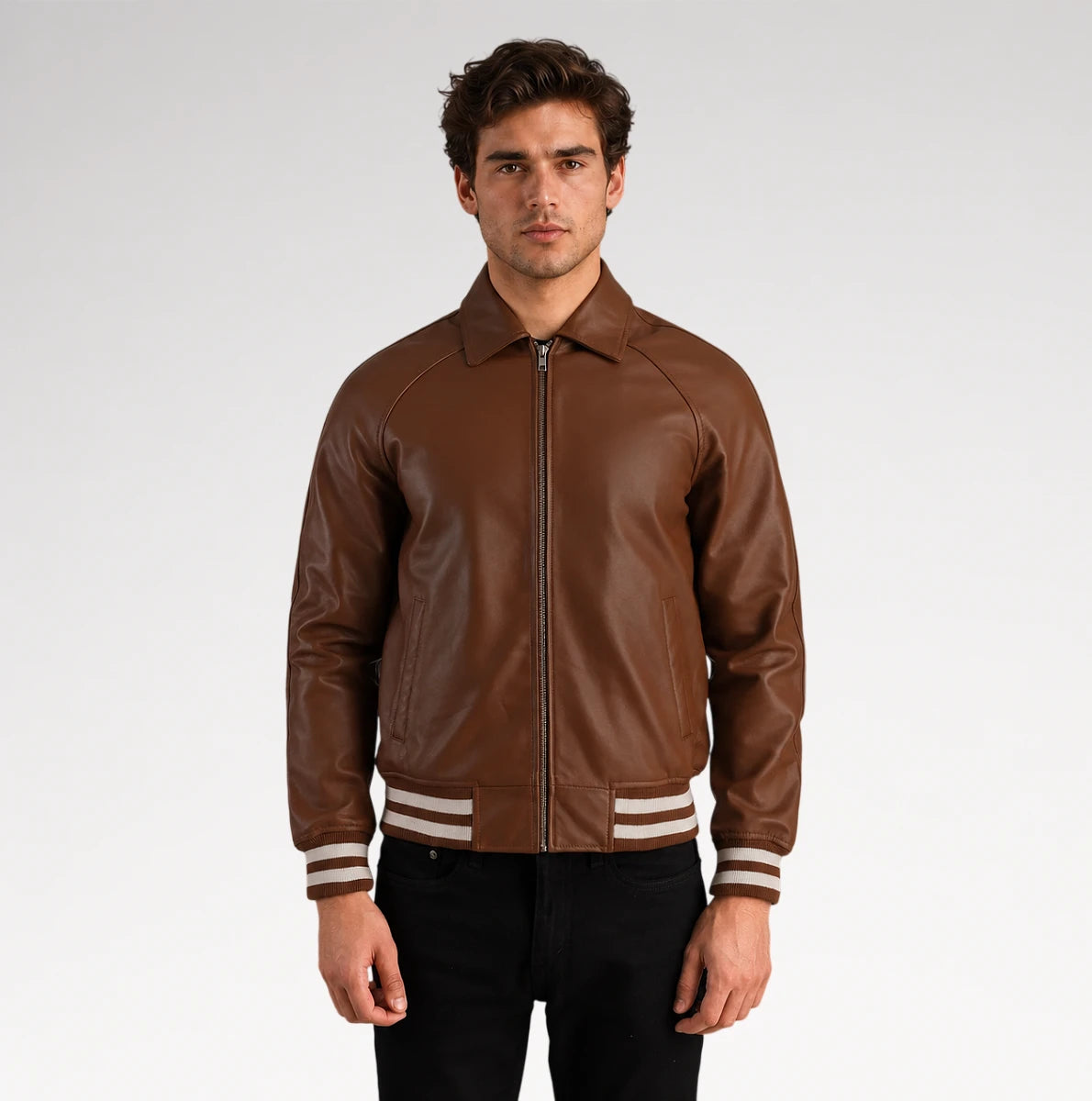 A man wearing a brown leather bomber jacket with cream and black striped ribbed cuffs and hem, paired with black pants, photographed against a light gray studio background.