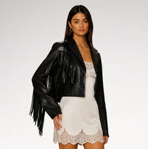A woman modeling a black faux-leather fringe jacket over a white lace-trim mini dress against a light gray studio background.