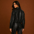 Person wearing a black leather jacket and pants against a brown background