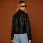 Woman wearing a black leather jacket and blue jeans against a brown background