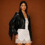 Woman wearing a black leather jacket with fringe and a white lace dress on a brown background