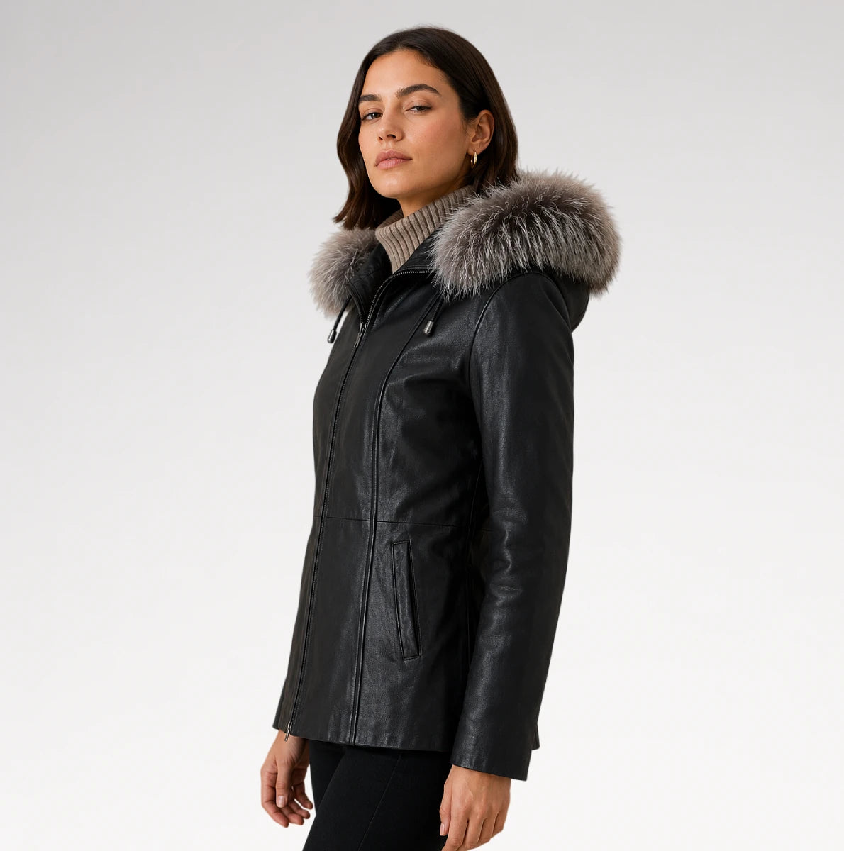 A woman wearing a black faux-leather parka jacket with a large gray fur-trimmed hood, photographed against a plain light gray studio background.